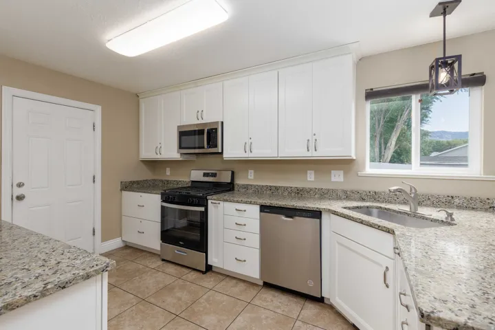 Kitchen featuring stainless steel appliances, white cabinetry, granite countertops, and tile flooring