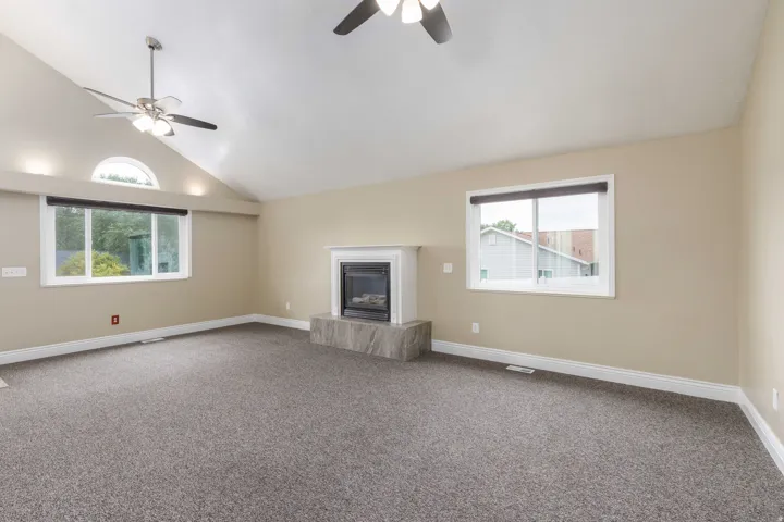Living area featuring a vaulted ceiling with two ceiling fans, a fireplace with a white mantel and stone-finish hearth, and multiple windows