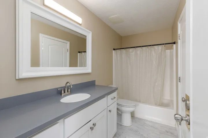 Bathroom featuring a white vanity with gray countertop, a white framed mirror, and a full bathtub with shower