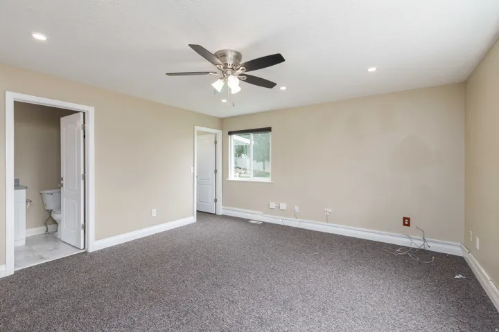 Spacious room featuring neutral wall tones, gray carpeting, a ceiling fan with integrated lighting, recessed lighting, and a window with outdoor landscaping visible