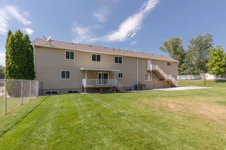 Rear exterior featuring tan siding, a ground-level deck with white railings, a concrete patio, and a chain-link fence