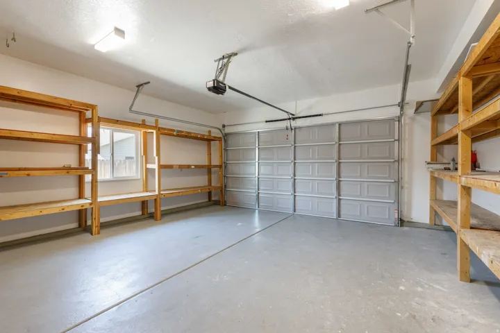 Spacious garage featuring a concrete floor, two garage doors, built-in wooden shelving, and a window for natural light