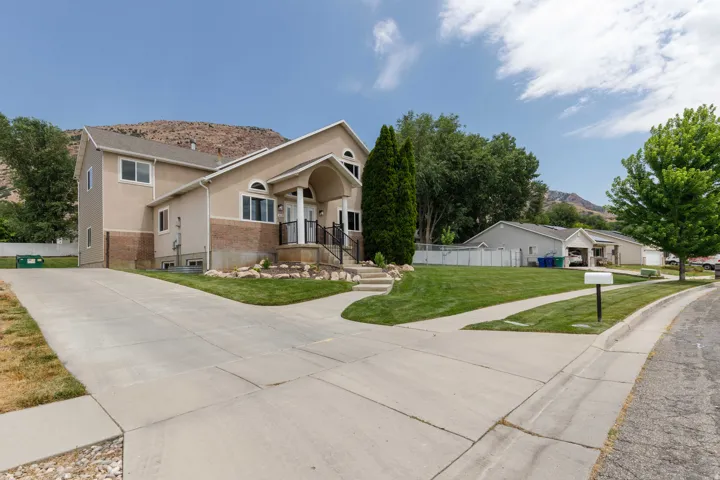Two-story stucco and brick exterior featuring a covered entry porch with columns, a multi-car concrete driveway, a manicured lawn, and mature landscaping