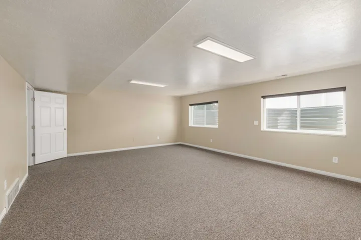 Spacious room featuring neutral carpeting, light beige walls, and two large windows with roller shades