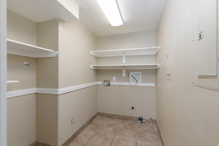Utility room featuring a fluorescent ceiling light, extensive built-in shelving, tile flooring, and neutral wall tones