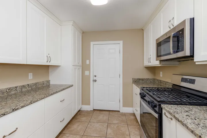 Kitchen featuring white shaker-style cabinetry, granite countertops, stainless steel microwave, and a gas range
