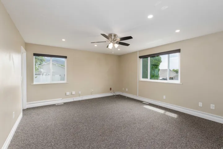 Spacious room featuring neutral paint, gray carpet, two windows, recessed lighting, and a ceiling fan with integrated lighting