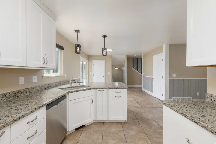 Kitchen featuring white cabinetry, light-toned granite countertops, stainless steel appliances, and tile flooring
