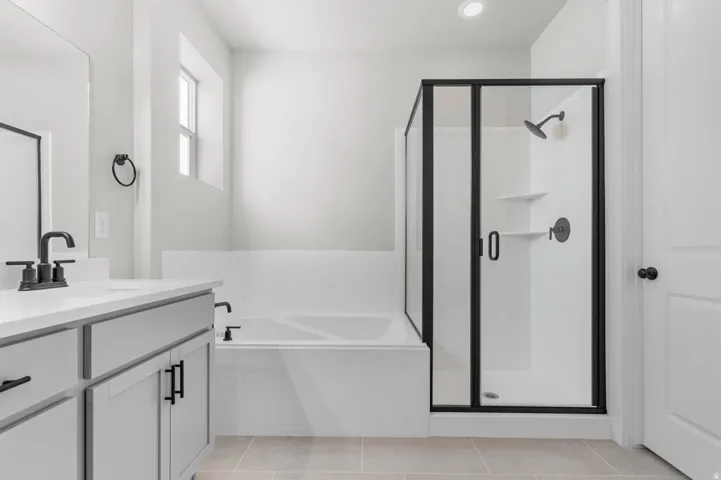 Bathroom featuring a single vanity with stone-finish countertop, light gray cabinetry, matte black hardware, a built-in tub, and a glass-enclosed shower with black framing
