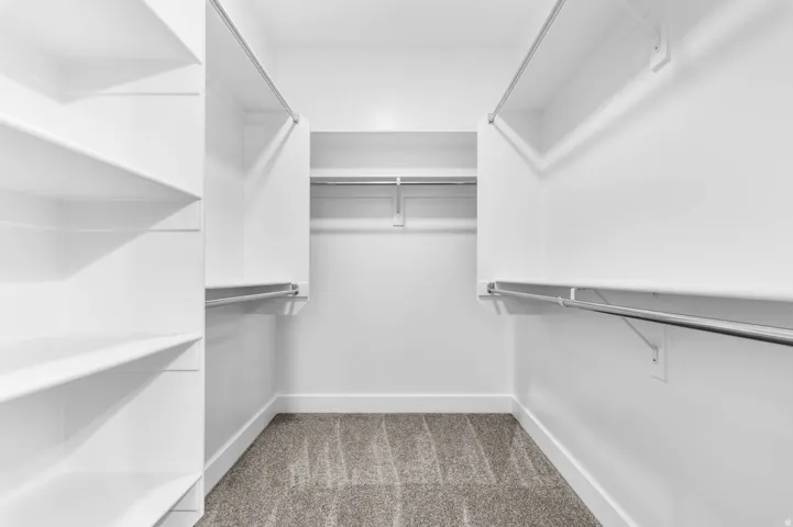 Walk-in closet featuring built-in shelving, multiple hanging rods, and neutral-toned carpeting