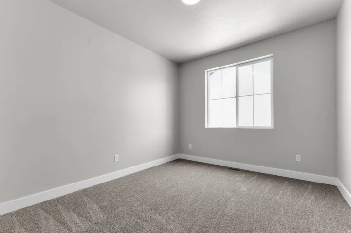 Neutral-toned room featuring a large window with grid panes, textured grey carpeting, white baseboards, and a recessed ceiling light