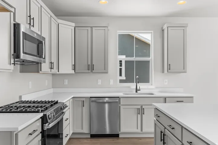 Contemporary kitchen featuring light gray cabinetry with black hardware, stainless steel appliances, and white countertops