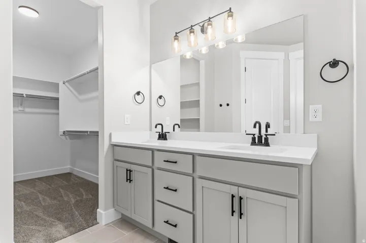 Dual vanity featuring light gray cabinetry, matte black hardware, and an expansive wall-mounted mirror
