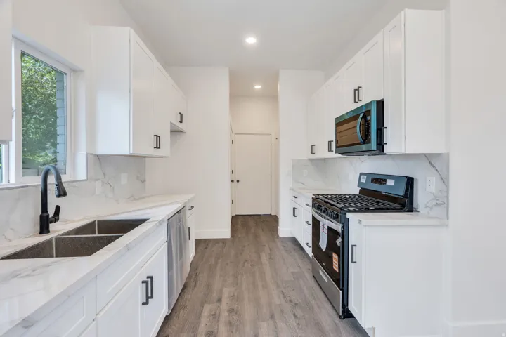 Contemporary kitchen featuring white cabinetry, stone-finish countertops with matching backsplash, and wood-finish flooring