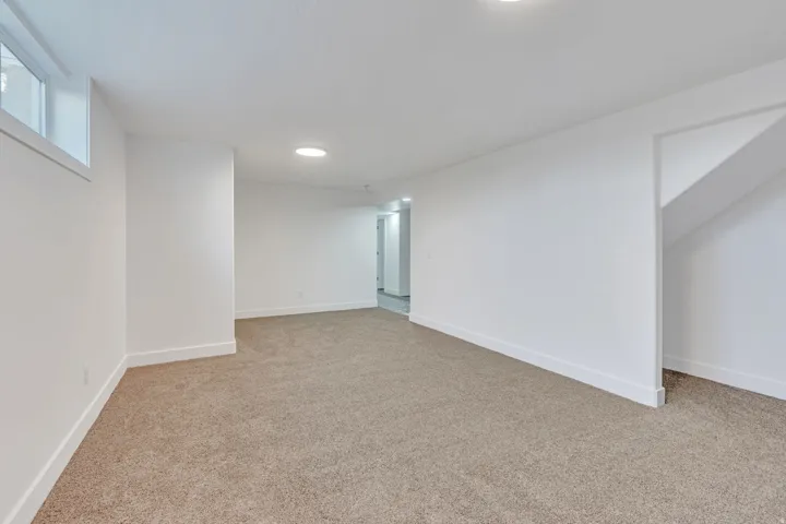 Spacious room featuring neutral carpet flooring, recessed lighting, and a white trim baseboard