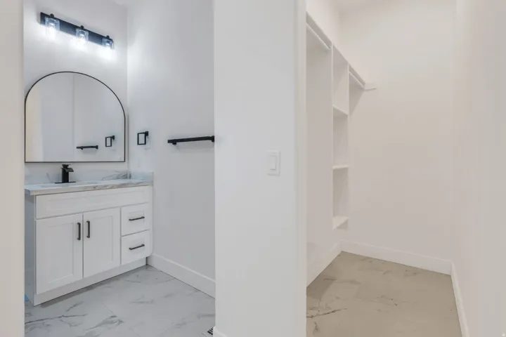 White vanity with black hardware, arched mirror, and stone-look countertop