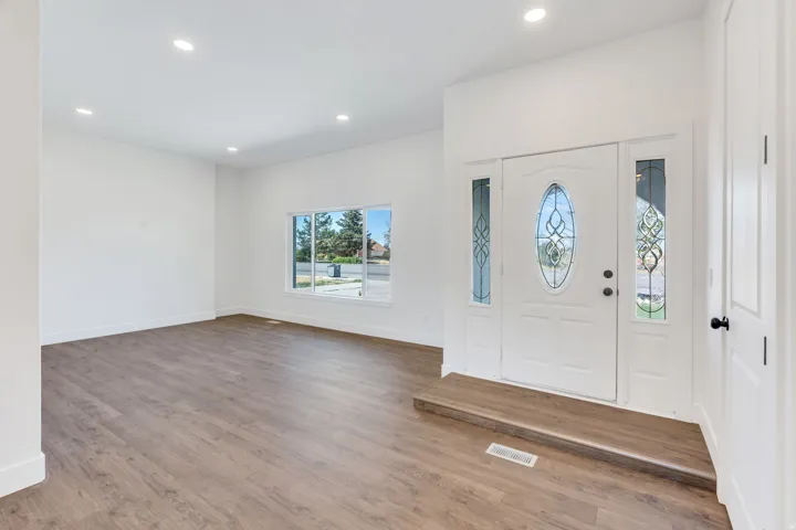 Entryway featuring an ornate oval-paneled door with decorative glass sidelights, wood-finish flooring, recessed lighting, and a large window