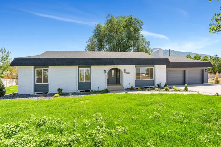 Ranch-style residence featuring a white brick facade with dark gray trim, a dark shingle roof, and an arched entryway