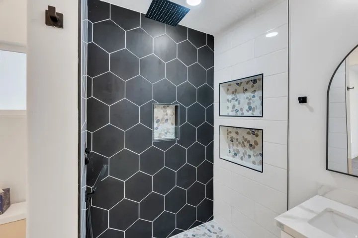 Shower featuring black hexagonal wall tiles, a built-in niche with pebble tile accents, white horizontally laid wall tiles, and a rainfall showerhead