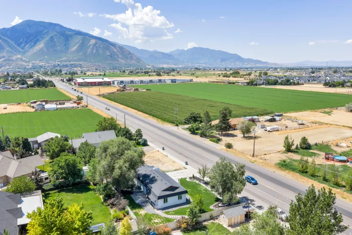 Aerial perspective showcasing the property's setting with distant mountains, expansive green fields, a paved roadway, and neighboring structures