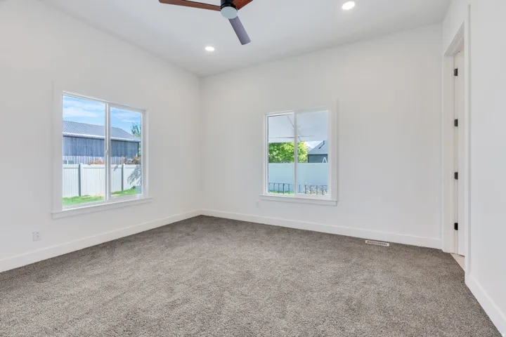 Spacious room featuring neutral carpeting, white walls, two large windows, recessed lighting, and a ceiling fan