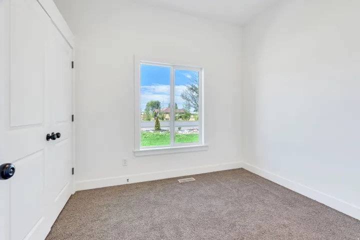 Bright interior space featuring a double-paned window, neutral carpeting, white baseboards, and a white two-panel interior door with matte black hardware