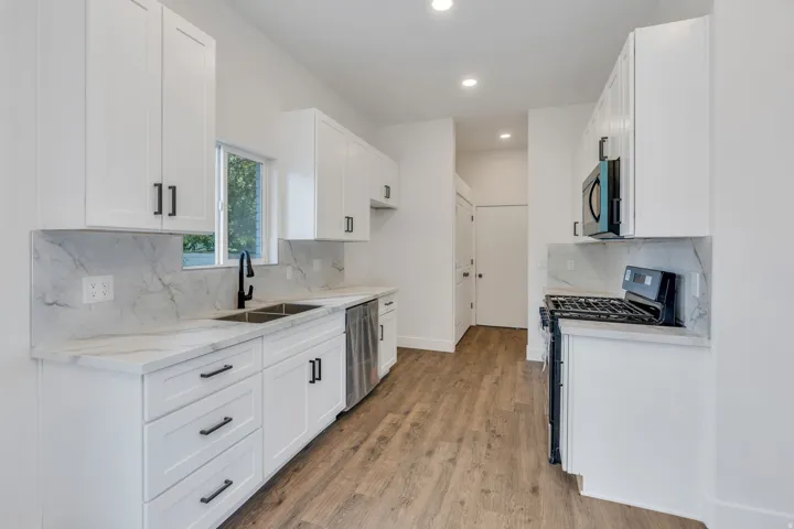 Modern kitchen featuring white shaker cabinetry with matte black hardware, stone-finish countertops, stainless steel appliances, and wood-finish flooring