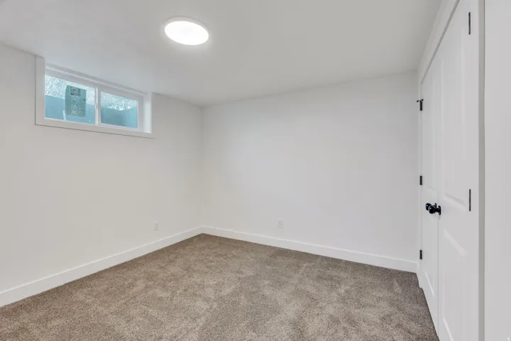 Bright room featuring neutral carpeting, a white egress window, and white interior doors with black hardware