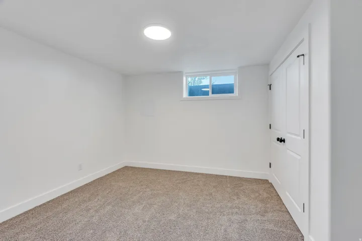 Neutral tone carpeting complementing bright white walls, showcasing a recessed window and a white panel door with matte black hardware