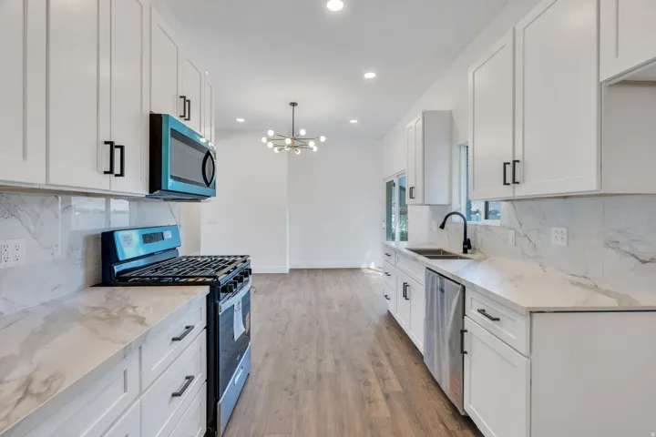 Modern kitchen featuring white shaker cabinetry with matte black hardware, stone-look countertops, a coordinating tile backsplash, stainless steel dishwasher, and a gas range
