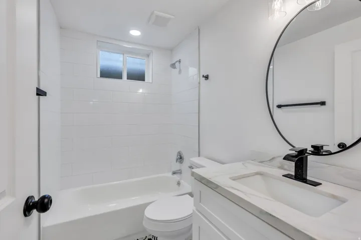 Contemporary bathroom featuring a white subway tiled shower, white bathtub, vanity with a rectangular undermount sink and stone-finish countertop, and matte black fixtures