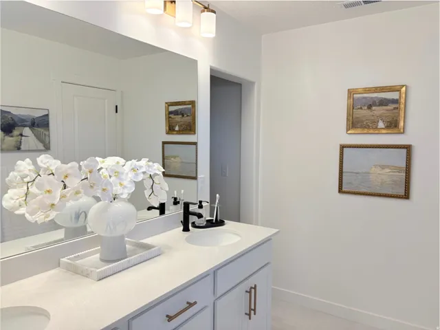 Bathroom vanity featuring a light-toned countertop with integrated sinks, light gray cabinetry, and matte black plumbing fixtures