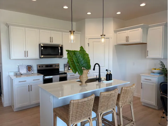 Kitchen featuring white shaker cabinetry, stainless steel appliances, a center island with a black faucet and undermount sink, and wood-finish flooring