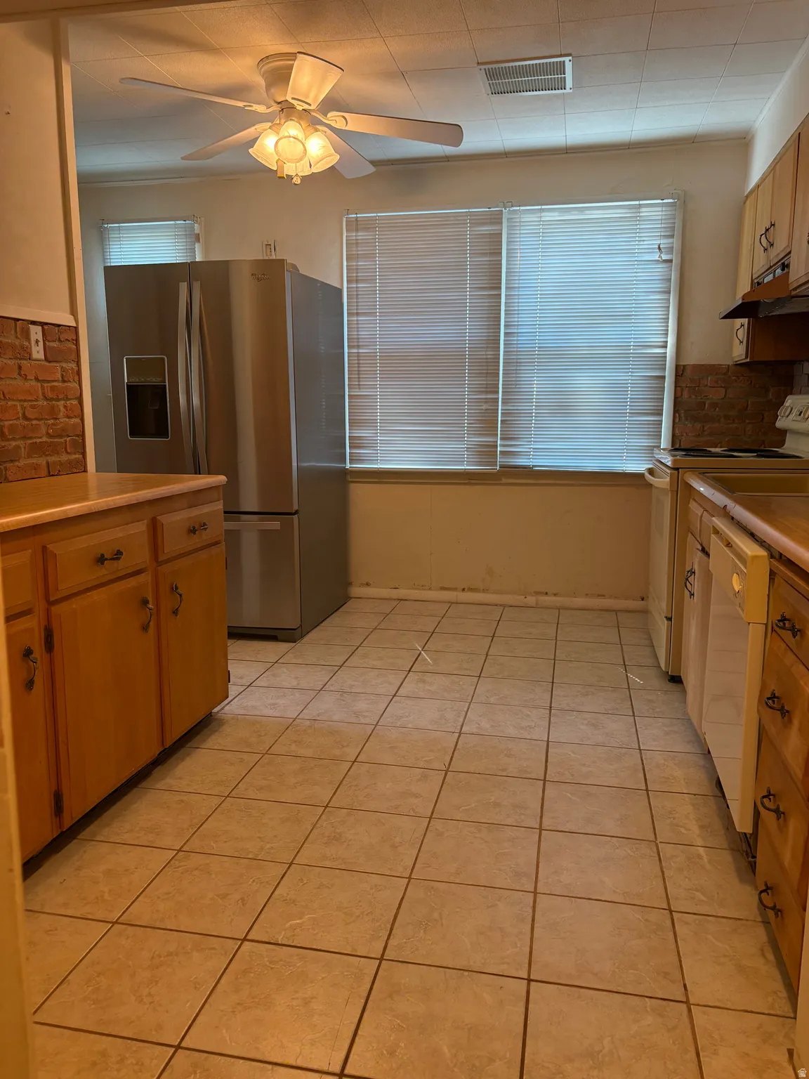 Tile flooring, wood-finish cabinetry, stainless steel refrigerator, brick-finish backsplash, ceiling fan with integrated lighting