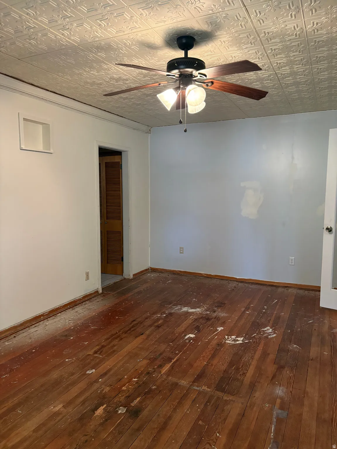 Spacious room featuring hardwood flooring, ceiling fan with integrated lighting, textured tin ceiling, and multiple wall outlets
