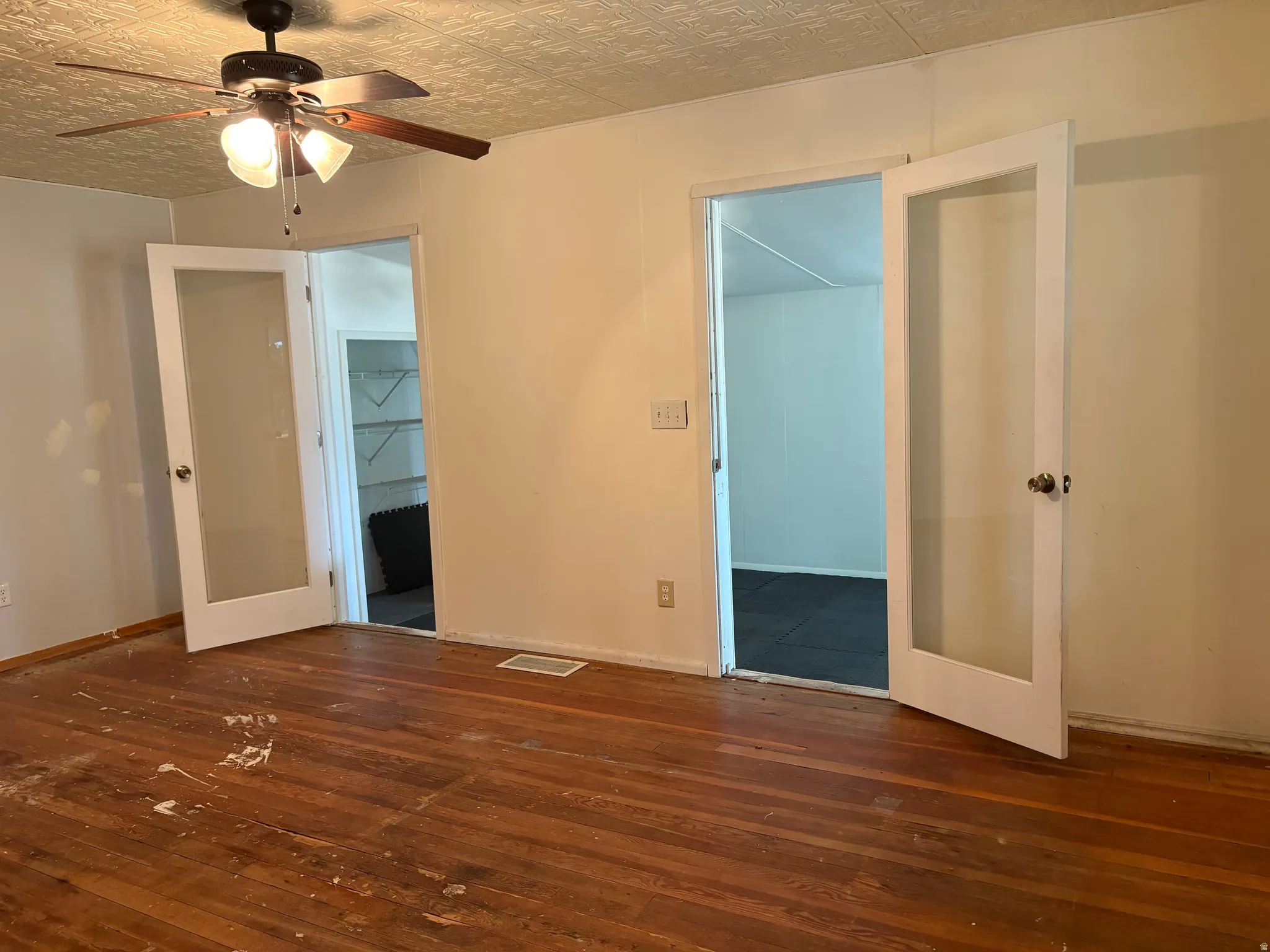 Spacious interior featuring gleaming wood-finish flooring, ceiling fan with integrated lighting, and multiple white-framed glass doors providing natural light and access to adjoining spaces