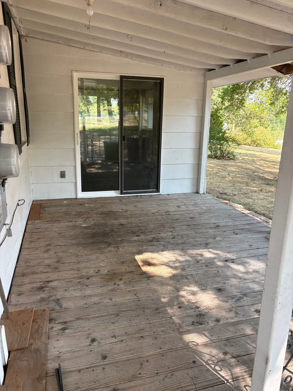 Covered outdoor living space featuring wood-finish flooring, white shiplap walls, exposed beam ceiling, and French doors opening to landscaped grounds