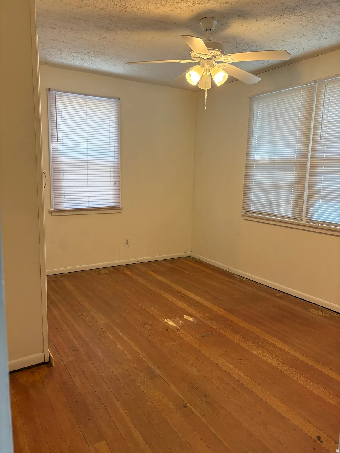 Bright corner bedroom with wood-finish flooring, ceiling fan with integrated lighting, and dual windows providing natural light