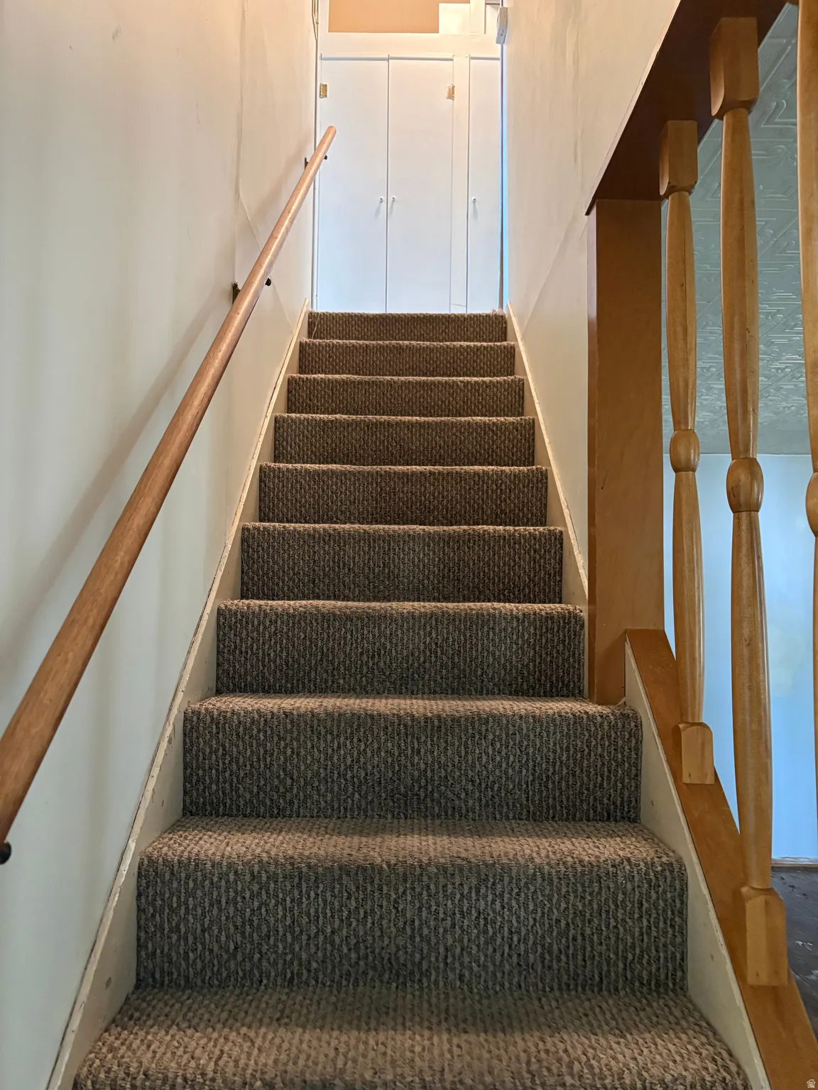 Staircase featuring textured carpet treads, a natural wood handrail, and white built-in storage at the landing