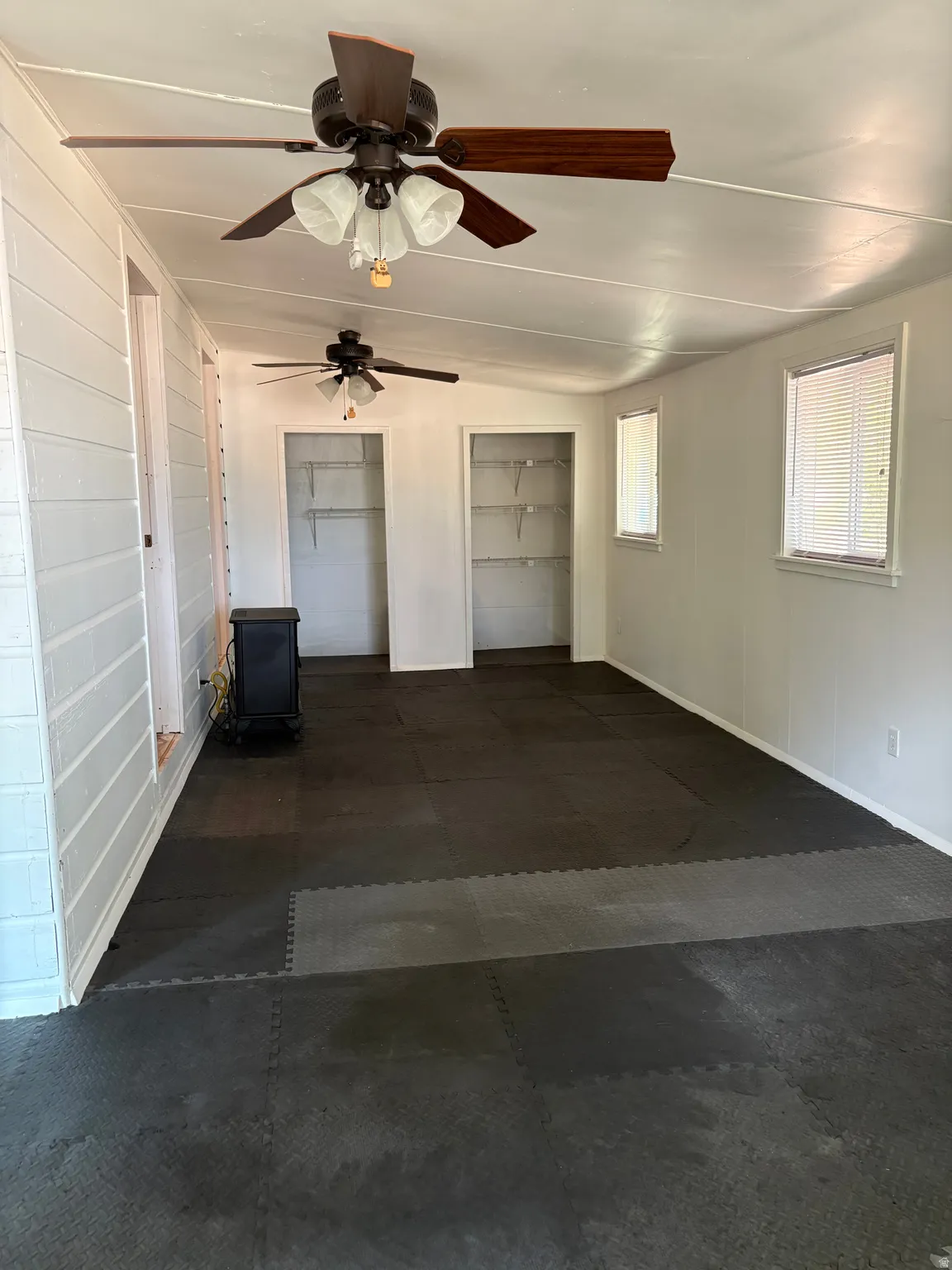 Spacious garage featuring epoxy-coated concrete flooring, dual ceiling fans with integrated lighting, two built-in storage closets, and abundant natural light from multiple windows