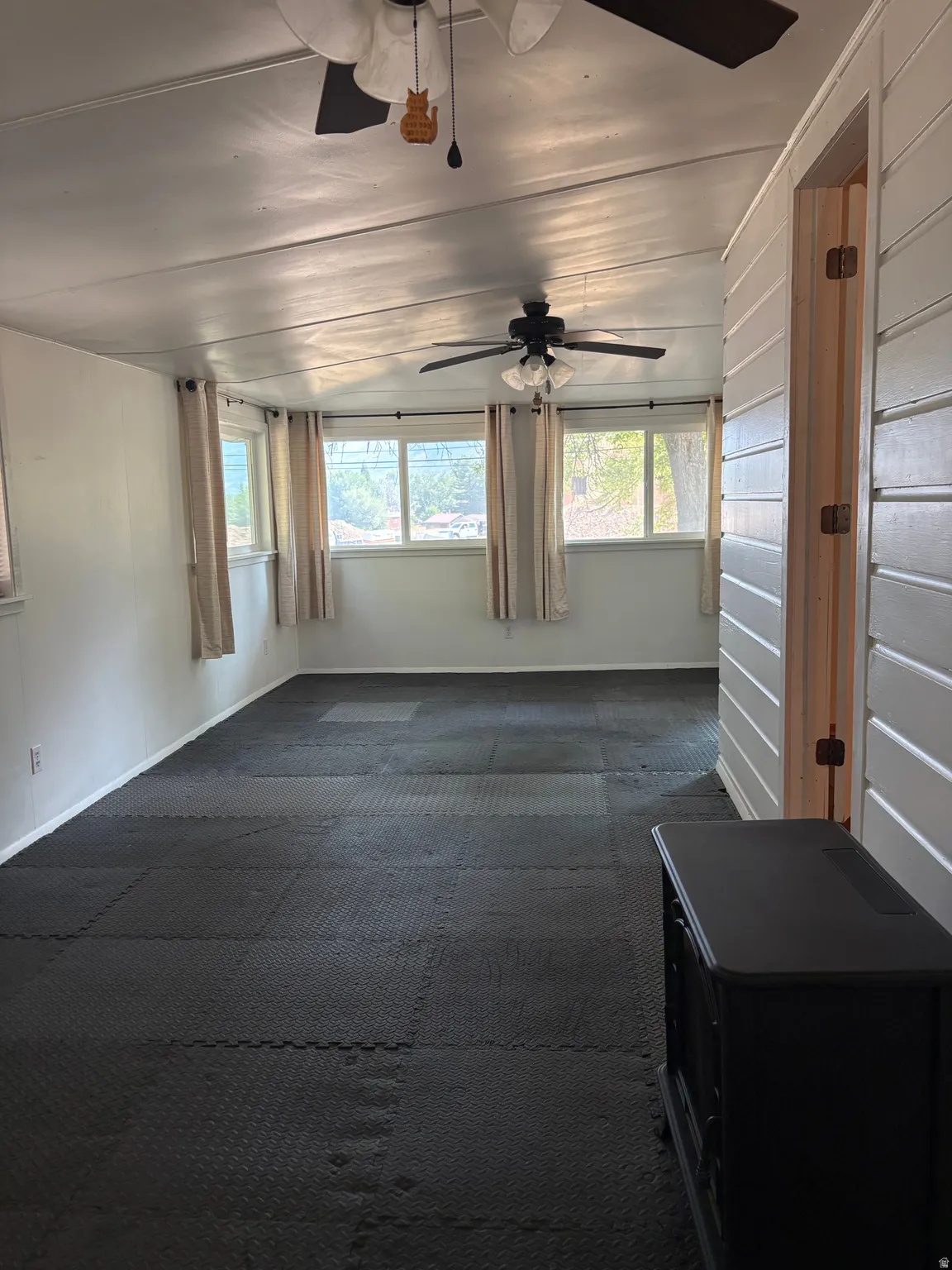 Spacious room featuring multiple windows, two ceiling fans, and dark interlocking floor tiles