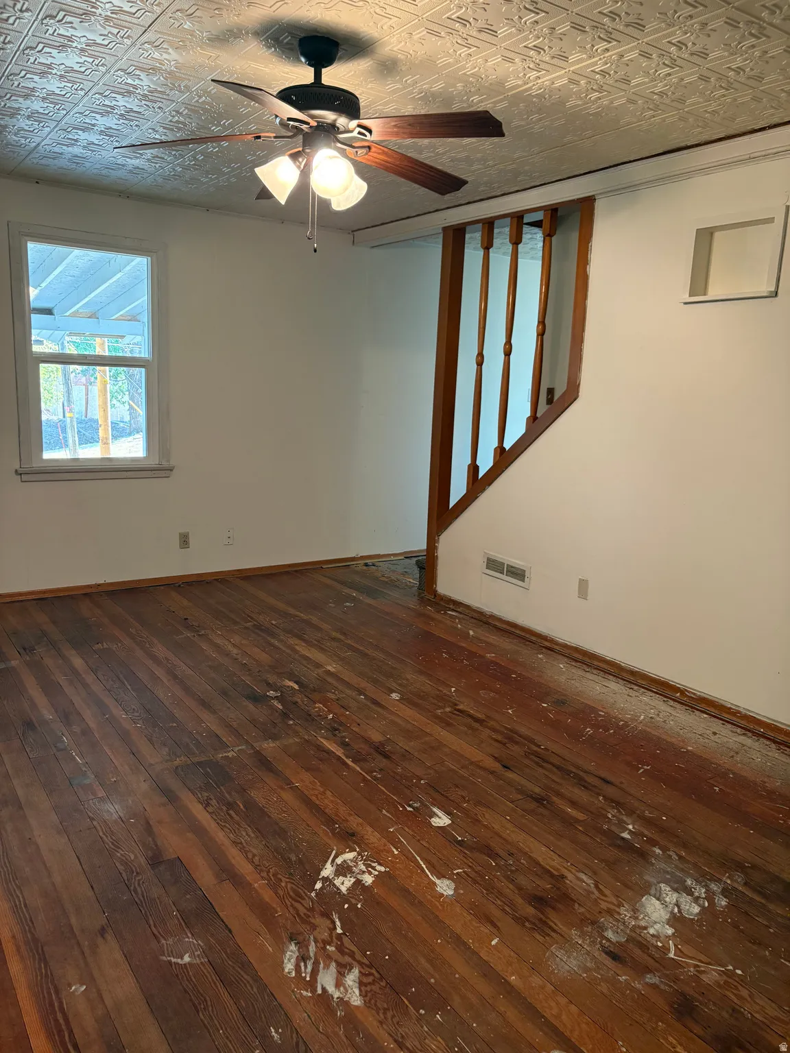 Hardwood flooring with a natural finish, textured ceiling, ceiling fan with integrated lighting, and a wood banister