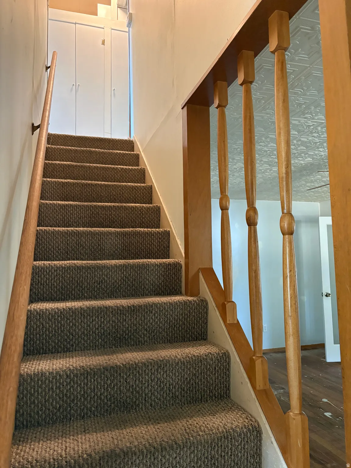Staircase with neutral-toned carpeted treads, wood-finish railings and balusters, and white painted walls