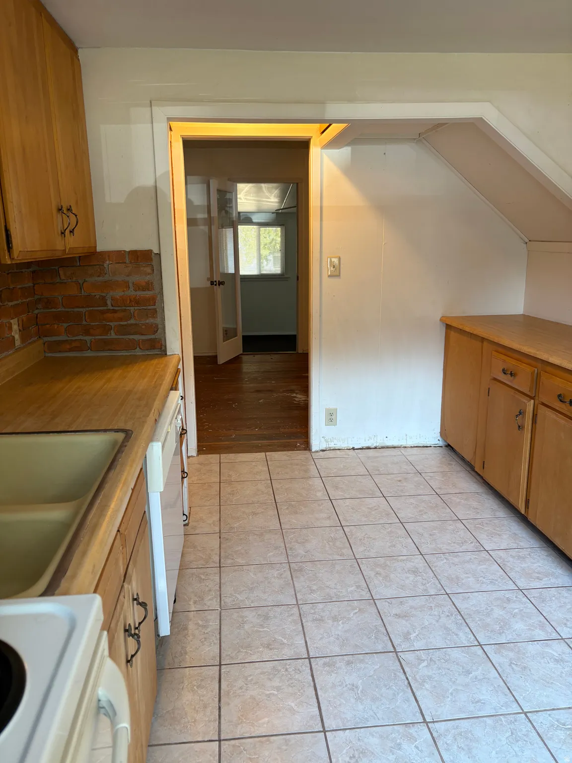 Light-toned tiled flooring, wood-finish cabinetry, and a brick backsplash