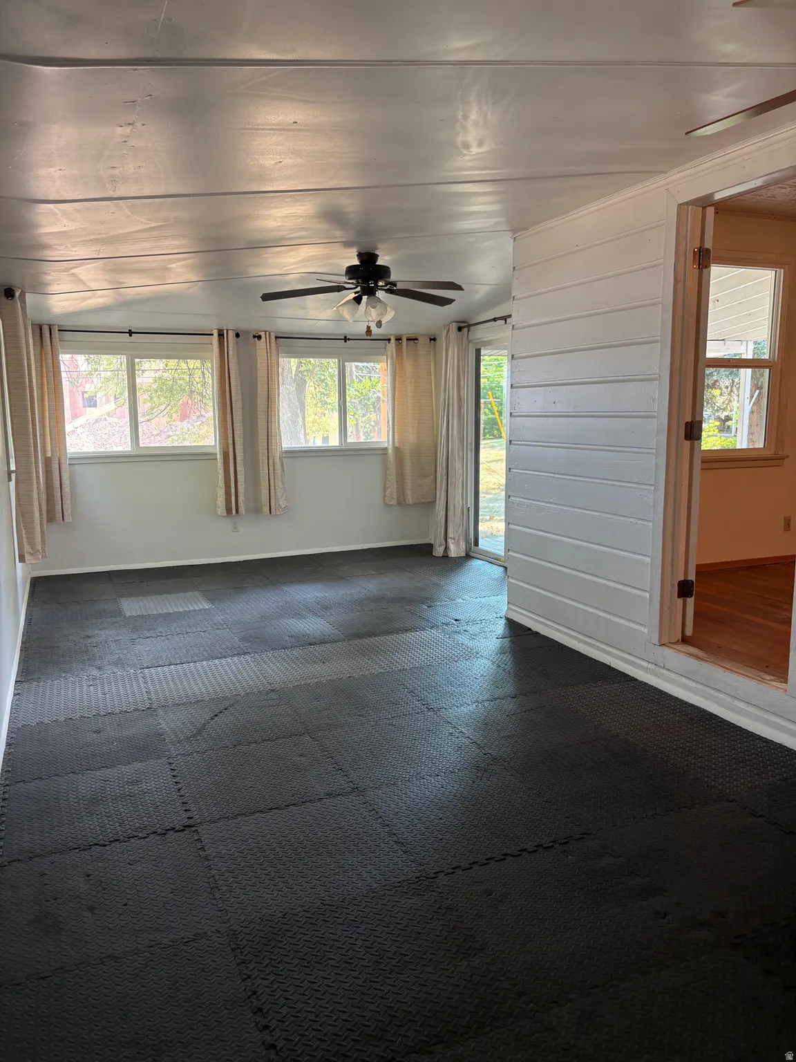 Expansive room featuring interlocking floor tiles, multiple windows, and a ceiling fan with integrated lighting