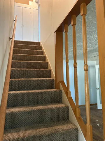Staircase with neutral-toned carpeted treads, wood-finish railings and balusters, and white painted walls