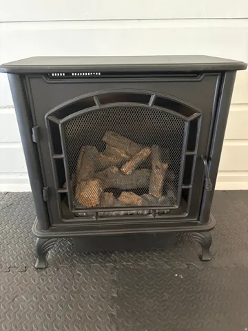 Freestanding cast-iron stove with arched mesh viewing window, decorative leg details, and integrated log storage—an elegant focal point offering both ambiance and supplemental heating capability