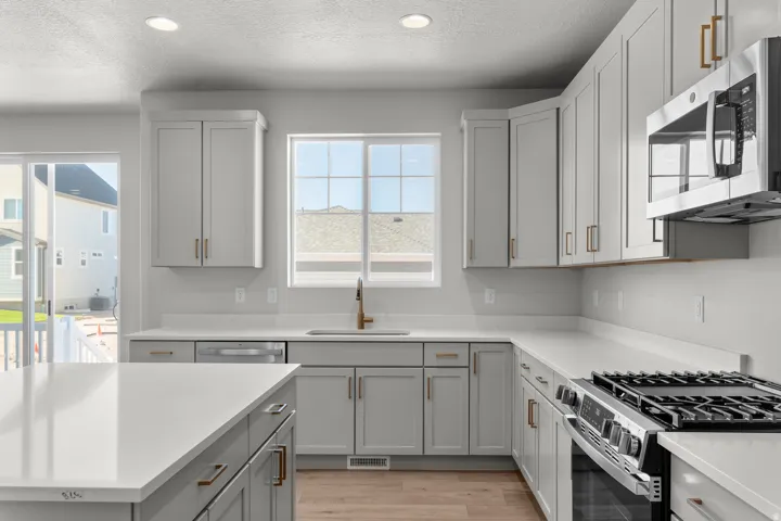 Kitchen featuring light gray cabinetry, white countertops, stainless steel appliances, wood-finish flooring, and a sliding glass door