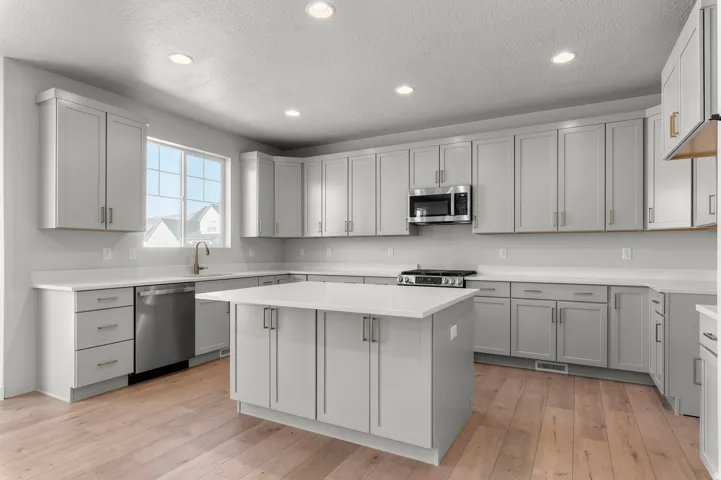 Spacious kitchen featuring gray shaker-style cabinetry, white countertops, stainless steel appliances, a central island, and wood-finish flooring