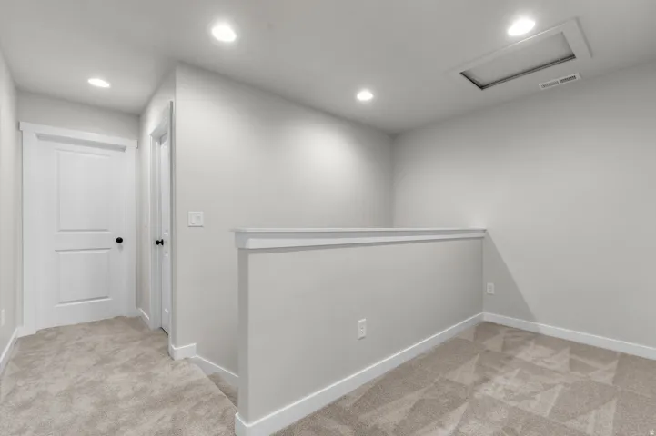 Recessed ceiling lighting, light gray wall paint, off-white trim, gray carpet flooring, and a white interior door